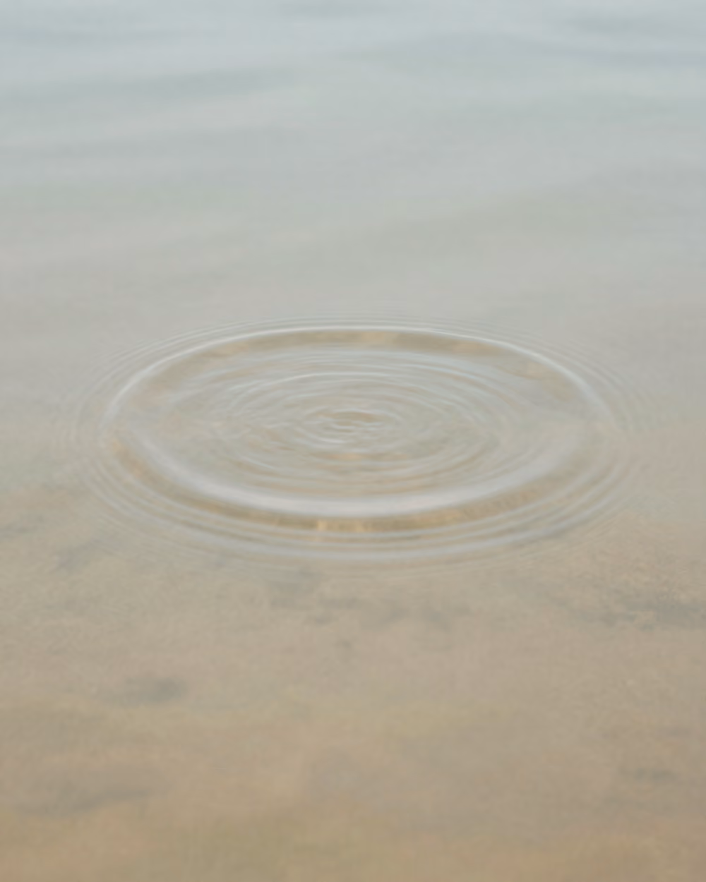 Ruhige Makroaufnahme einer einzelnen Welle auf heller, stiller Wasseroberfläche. KI-generierte Darstellung.